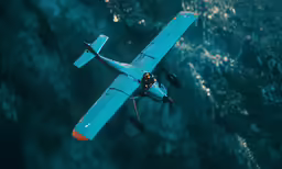 a small blue airplane flying over the ocean