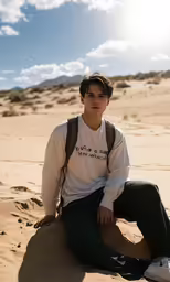 a young man sits on the sand dunes