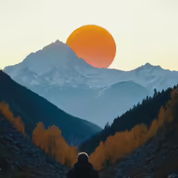person sitting at the edge of a mountain with the sun shining down