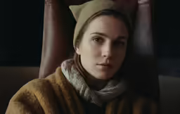 a girl is sitting in a chair wearing a sweater and scarf