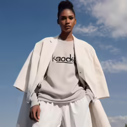 a woman in a white coat poses against a blue sky