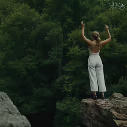 a woman standing on top of a rock holding her hands in the air