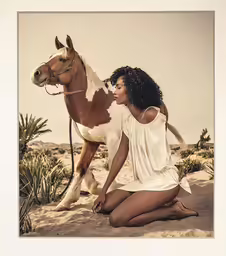 a woman with her horse sitting on a dune in a desert