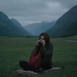 a woman sitting in a field taking a picture with her camera