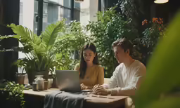 a couple sit at an outdoor restaurant using laptop