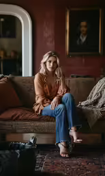 a young blond woman sitting on the couch with her feet on a wooden table
