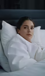 an attractive young woman laying in a bed under a blanket