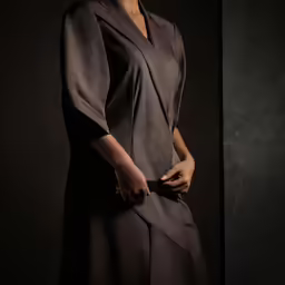 a woman in brown is standing next to a black wall