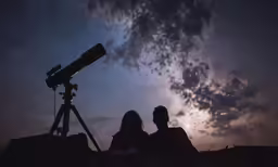 two people are sitting in the field as the stars are shining