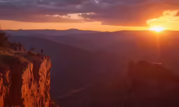two people stand on the edge of a cliff at sunset