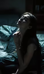 a woman that is sitting on a bed with her hands together