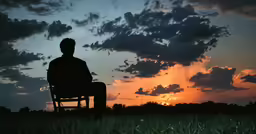 a silhouette of a man sitting in an open field