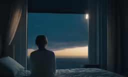 a woman sitting in the bed looking out of a window at night