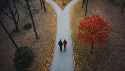 two people walking down a road in the middle of trees