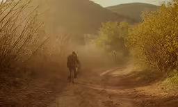 a man rides his bike down the dirt road