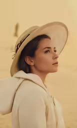 a young girl wearing a hat and coat on a beach