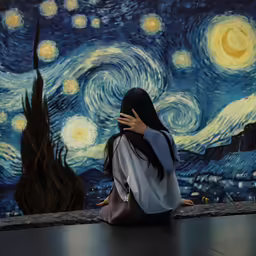 a girl sitting on the ground in front of a starr night painting