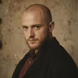 man with bald head standing against stone wall