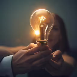 a woman holding a glowing light bulb up to the camera