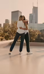 two women in jeans embracing outside near cityscape