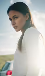 a woman in white shirt standing near car and sky