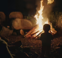 a young child stands in front of a pile of logs