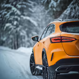 orange mercedes gle suv driving through the snowy forest