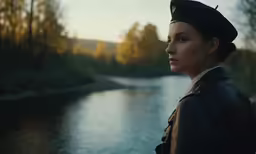 woman in uniform standing by a river at sunset