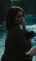 a woman with a camera sitting on a chair next to the water