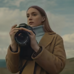 a woman holds up an old camera on the grass