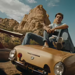 a young man sits on top of an old car