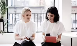 two women sitting down looking at a tablet