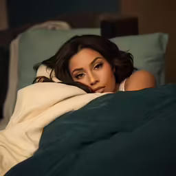a woman sitting on a bed under a blanket
