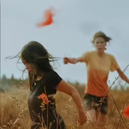 two little girls run through a field of tall grass