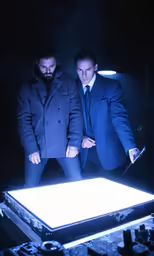 two men with their hands on their hips looking down at a piece of metal