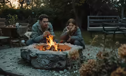 two people sitting around a fire pit in the dark