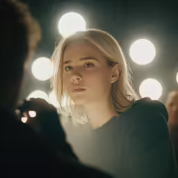 a blonde woman is staring at someone while sitting in a dimly lit room