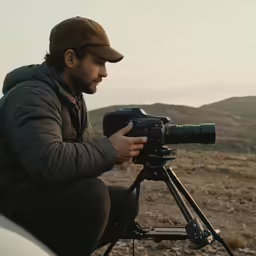a man sitting next to a car holding a camera