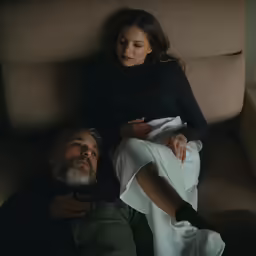 an older couple lies on the couch beside a woman who is hugging him