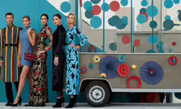 four models in colorful fashion stand next to a truck