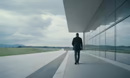 a man walking along an empty street past large glass windows