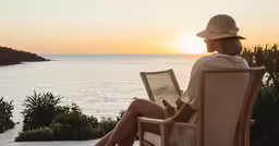 a woman sits alone at an outside patio overlooking the ocean