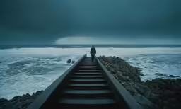 a man stands on the end of a boardwalk as rain is coming in over the ocean