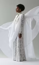 a woman stands in white and wears a white coat