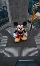 a mickey mouse balloon sitting on the sidewalk of a city street