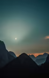 sun over mountains with bright clouds above