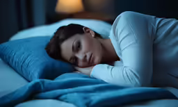 a young woman laying in bed with blue sheets on her