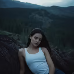 the woman sits against a wall in the mountains