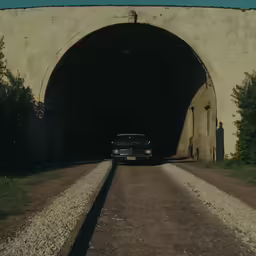 an older car driving through a tunnel on a dirt road