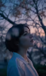 a girl looking up at the sky with a tree behind her